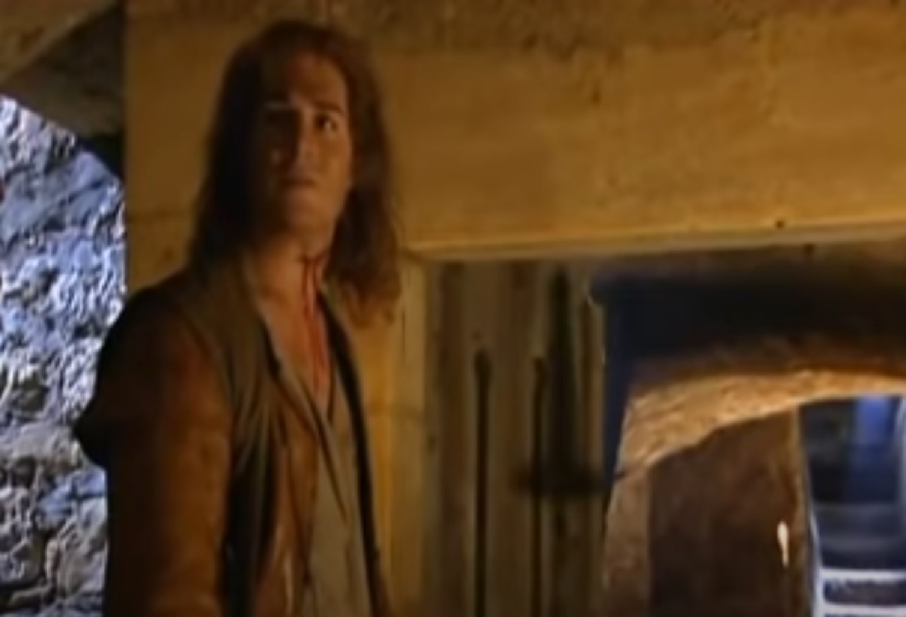 Screenshot: (Mark Umbers) Perkin Warbeck with long hair and brown shirt is looking at camera - from Princes in the Tower (2005).