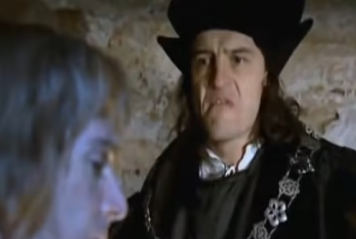 Screenshot: (Mark Umbers) Perkin Warbeck with long hair is talking with other  person in prison- from Princes in the Tower (2005).