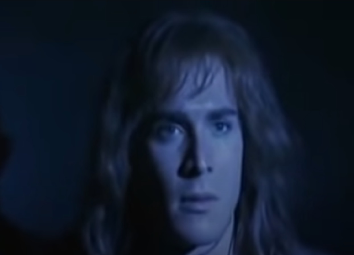 Screenshot: (Mark Umbers) Perkin Warbeck with long hair is looking at side - from Princes in the Tower (2005).