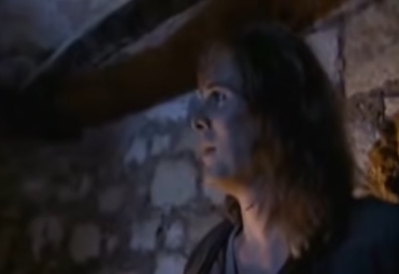 Screenshot: (Mark Umbers) Perkin Warbeck with long hair is looking at side in stone basement - from Princes in the Tower (2005).