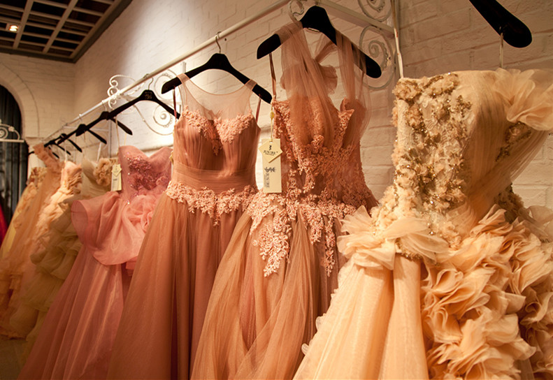 Multiple Ball Gowns hanging on a wall in a white brick wall room