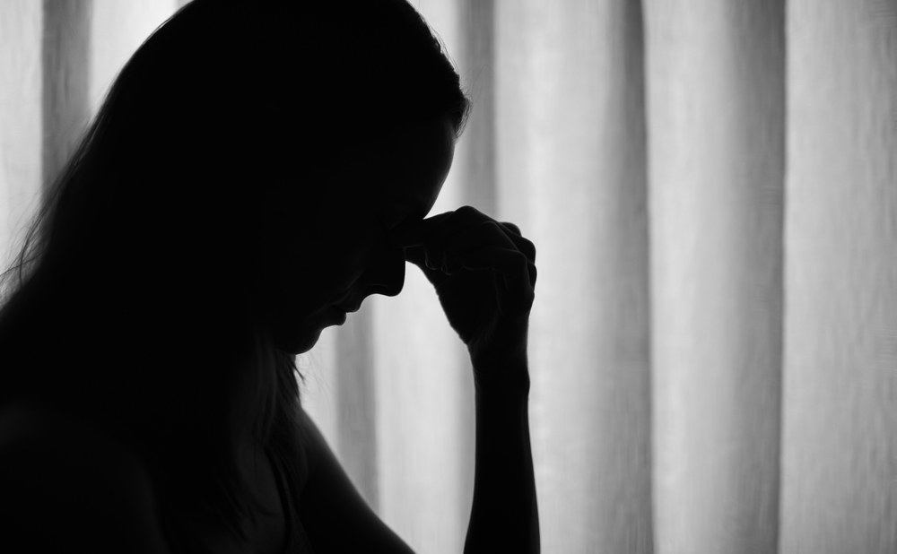 Sad stressed woman silhouette with hand over face next to window
