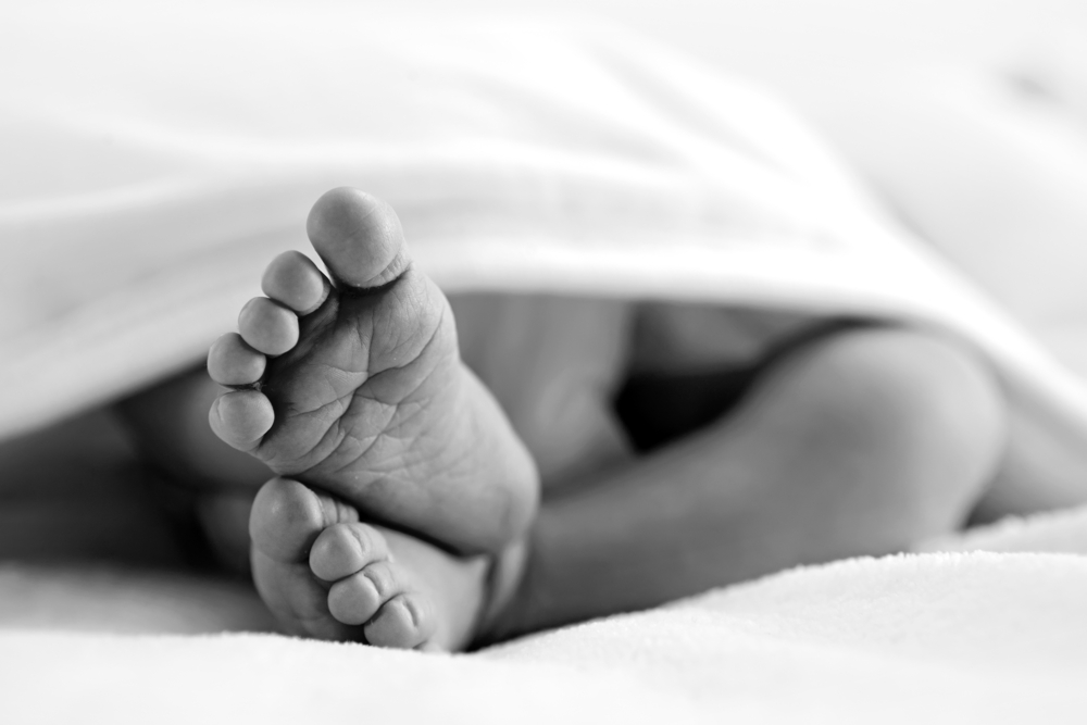 Grayscale photo of Newborn feet covered with white blanket