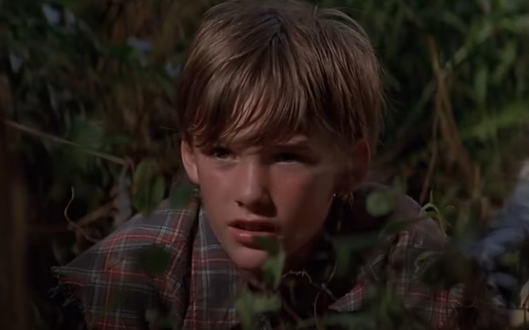 Screenshot of the actor Brad Renfro from the Movie The Client (1994) depicting a boy hiding behind the bushes