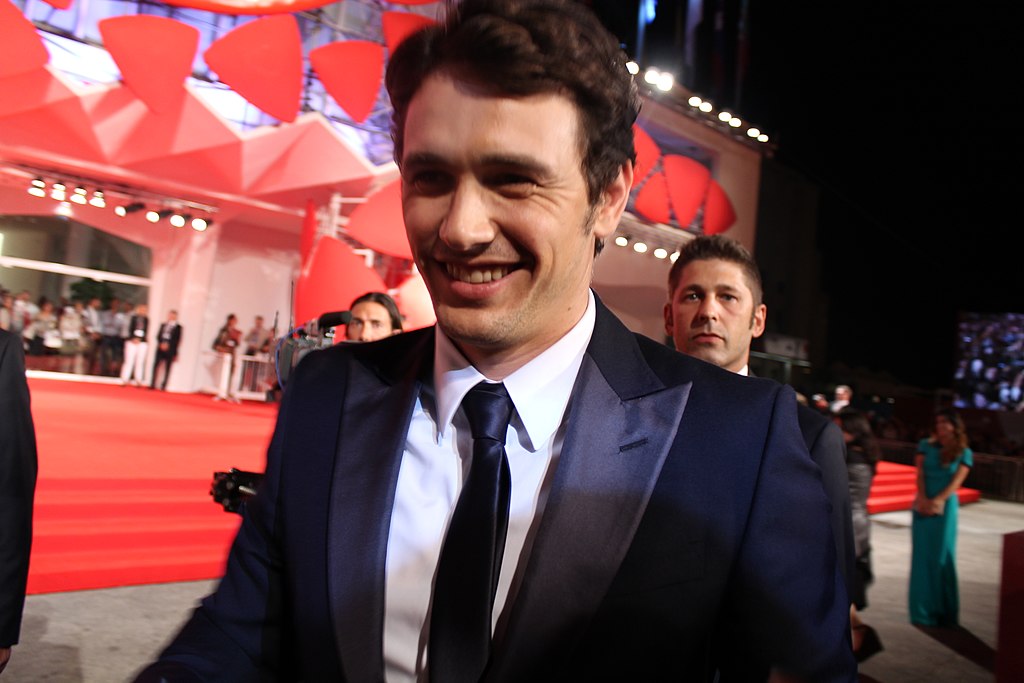Actor James Franco at the Venice Film Festival wearing a dark blue suit, smiling