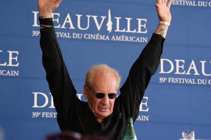 Director Larry Clark at the Deauville film festival wearing a black shirt sunglasses with his arms raised