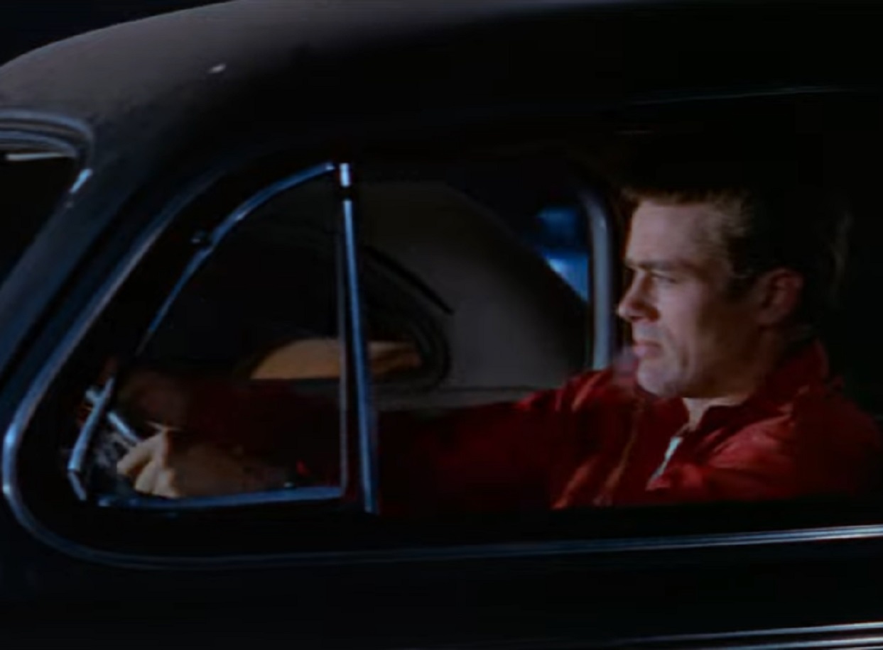 Screenshot: photo of James Dean wearing red jacket is driving a car - from Rebel Without A Cause (1955).