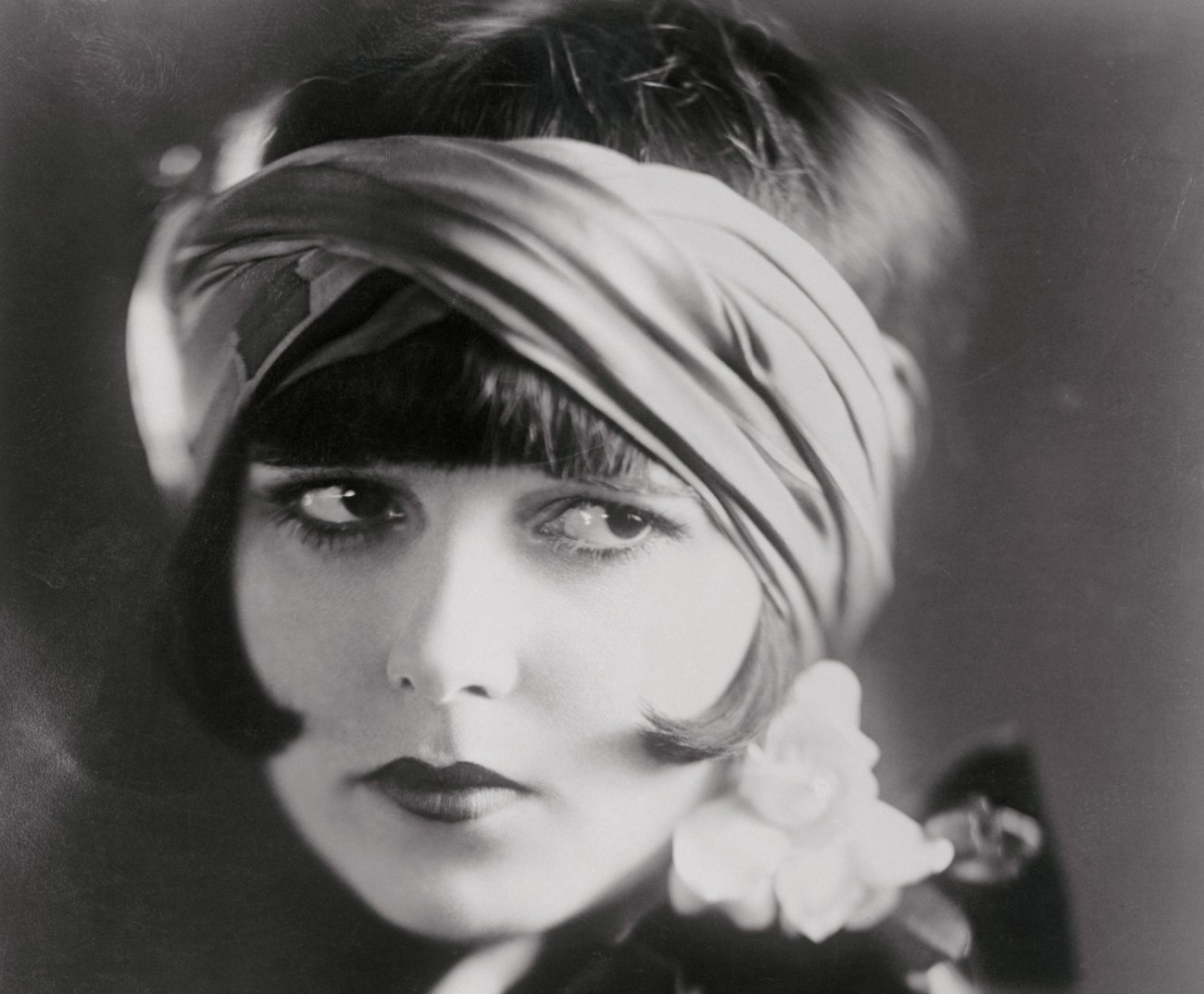 Grayscale Portrait Photo of the actress Louise Brooks, wearing a dress with white flower, facing the camera