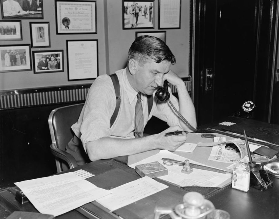 George Marshall sitting on a work table speaking to the phone, wearing white shirt