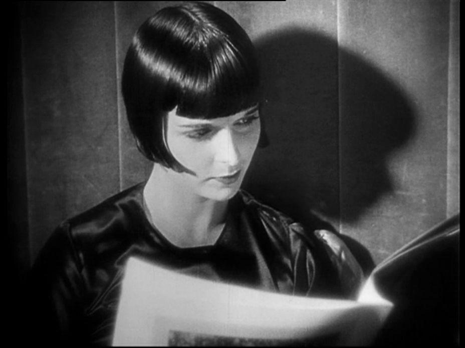 Grayscale Portrait Photo of the actress Louise Brooks, wearing black dress, reading newspaper