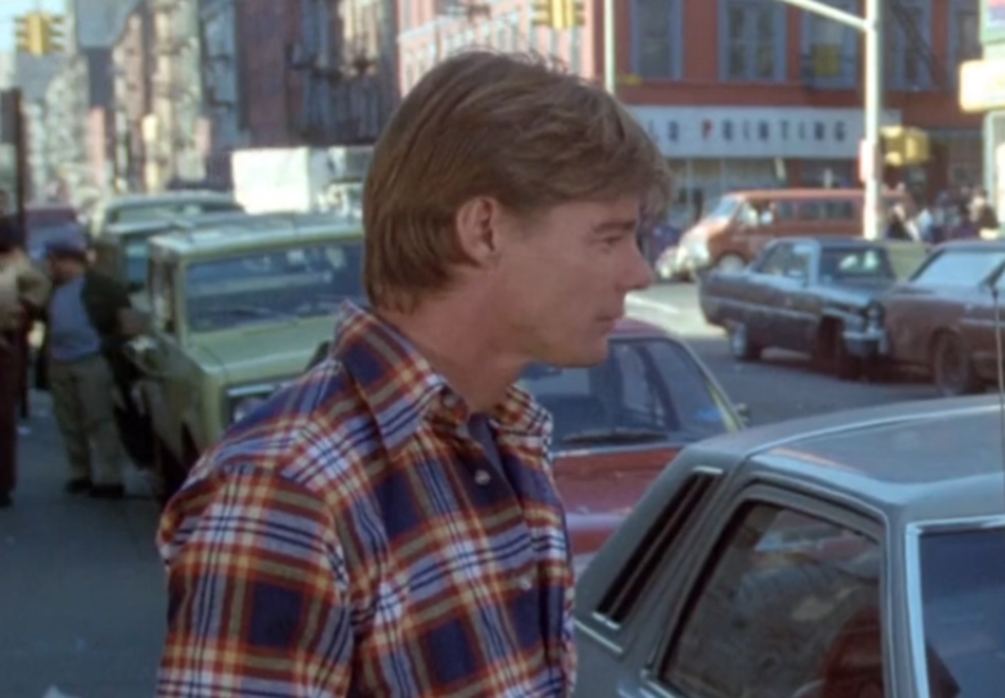 Screenshot: Jan-Michael Vincent wearing blue and red shirt is walking on the street - from Defiance (1980)