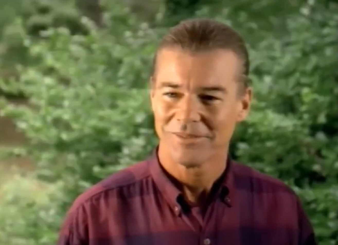 Screenshot: Jan-Michael Vincent wearing red shirt is looking at front and smiling - from Hidden Obsession (1993)