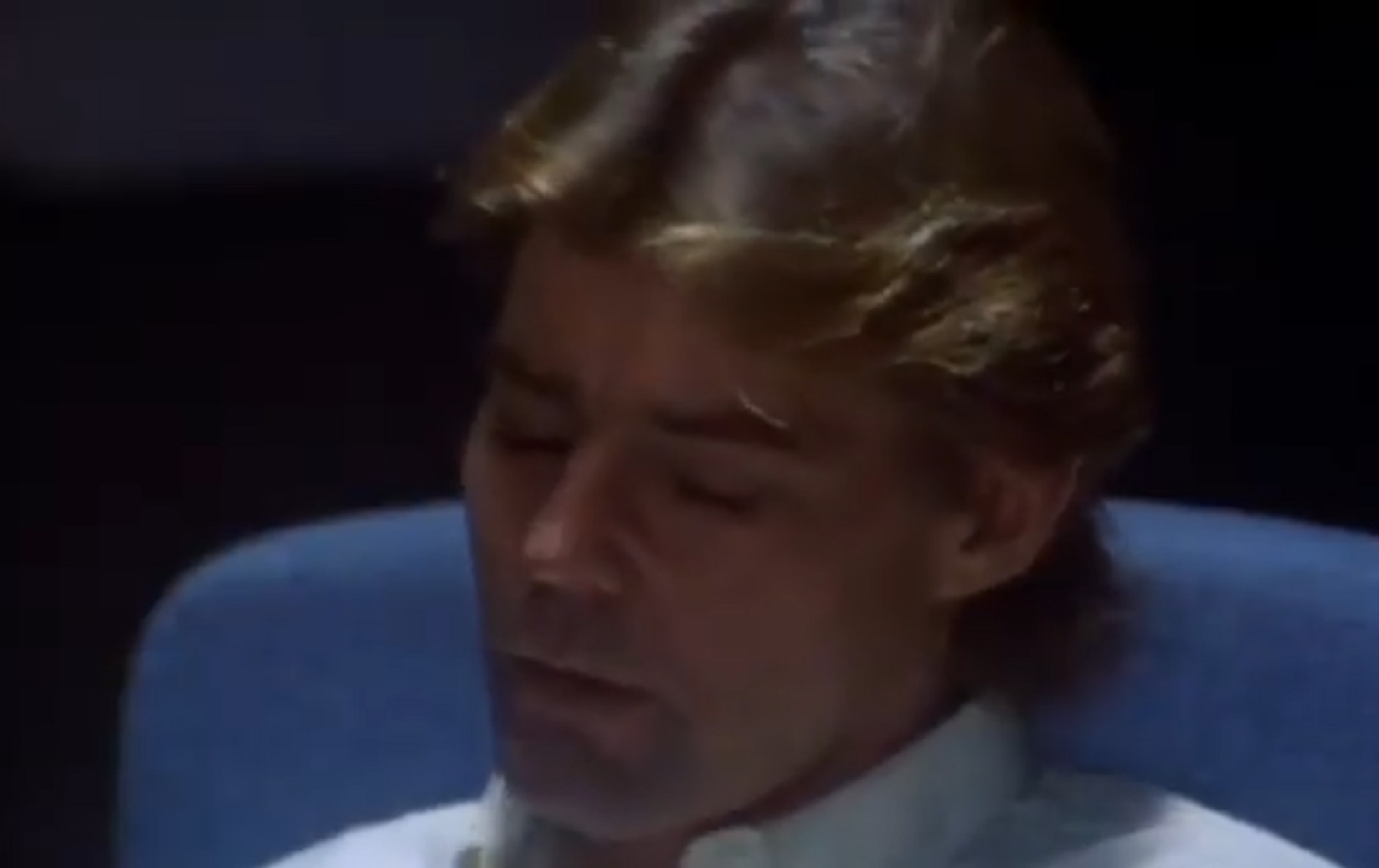 Screenshot: Jan-Michael Vincent wearing white shirt is looking down ,seating on the chair  - from Xtro Ii- The Second Encounter (1991)