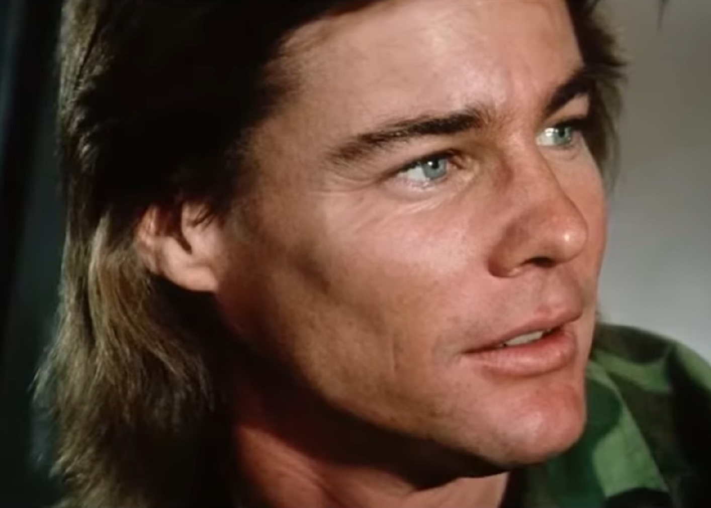 Screenshot: Jan-Michael Vincent wearing green shirt is smiling and looking at side - from Damnation Alley (1977)