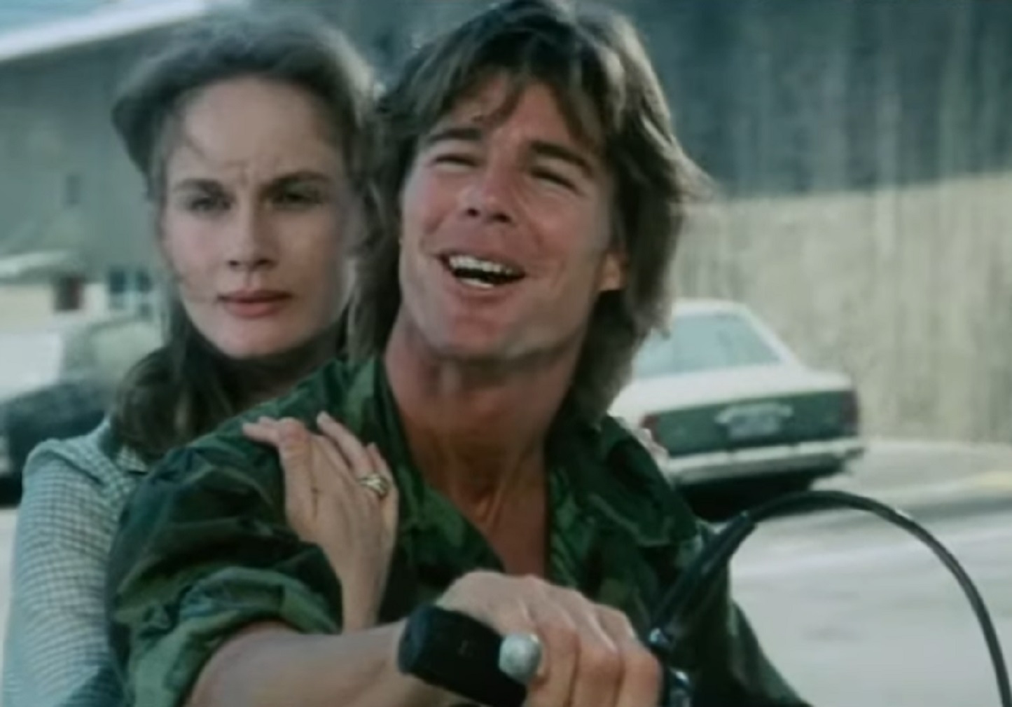 Screenshot: Jan-Michael Vincent wearing military uniform is on the bike with woman and smiling - from Defiance (1980)