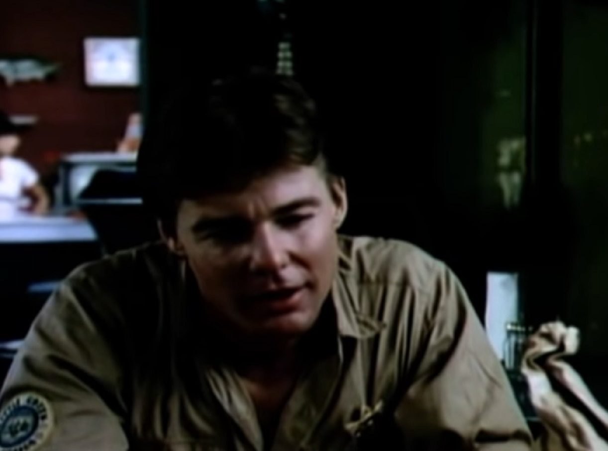 Screenshot: Jan-Michael Vincent wearing police shirt is seating on the table - from The Return (1980)