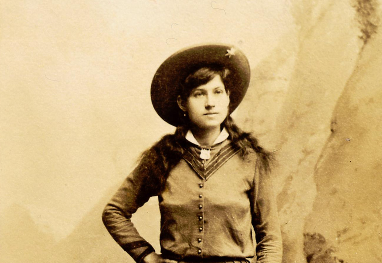 Grayscale Portrait photo of Annie Oakley, wearing a dress with and a hat