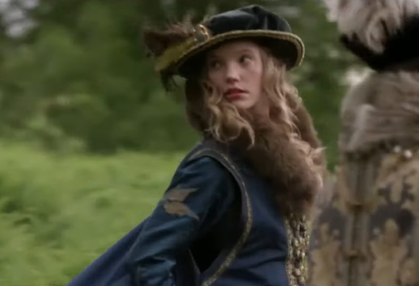 Screenshot of Catherine Howard with long hair wearing blue coat and hat is looking back - from The Tudors (2007–2010)