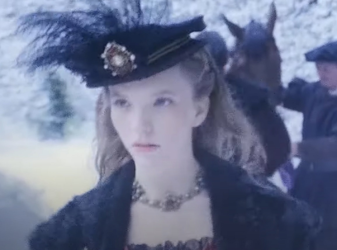Screenshot of Catherine Howard with long hair wearing black coat and hat is looking at front - from The Tudors (2007–2010)