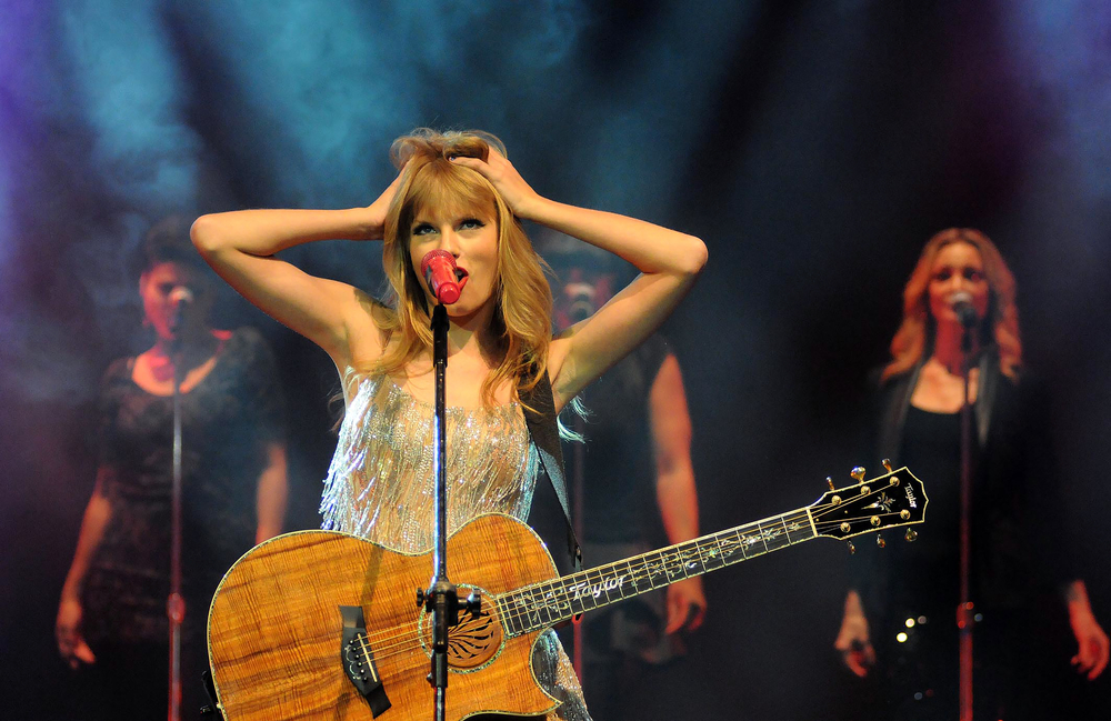 Singer Taylor Swift during her show at the HSBC Arena in Rio de Janeiro, Brazil, with a guitar wearing a shiny dress, arms on her head