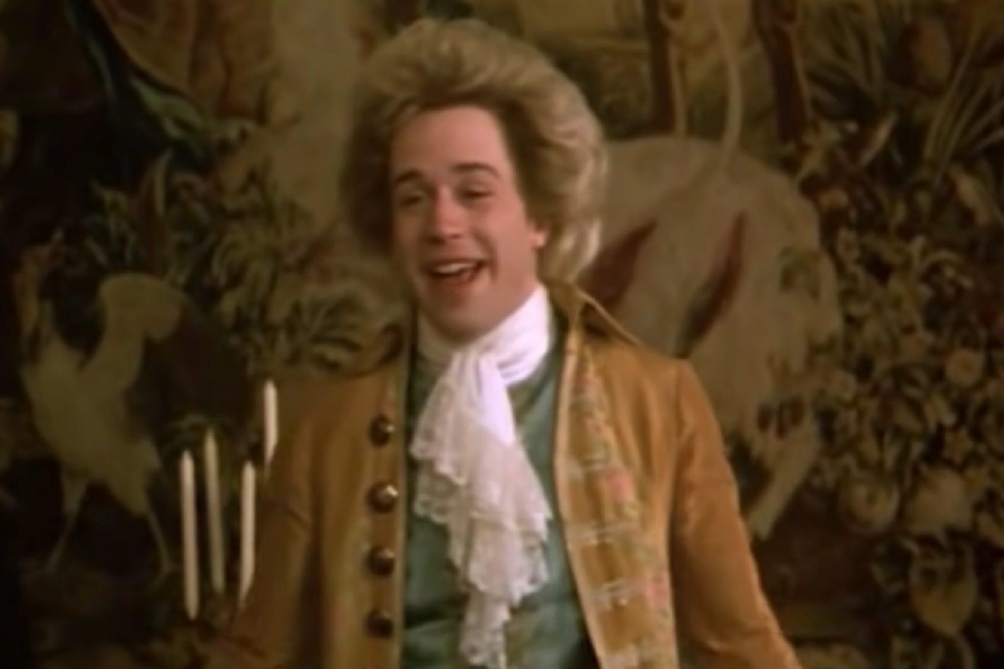 Screenshot: Wolfgang Amadeus Mozart in brown jacket is smiling - from Amadeus (1984)