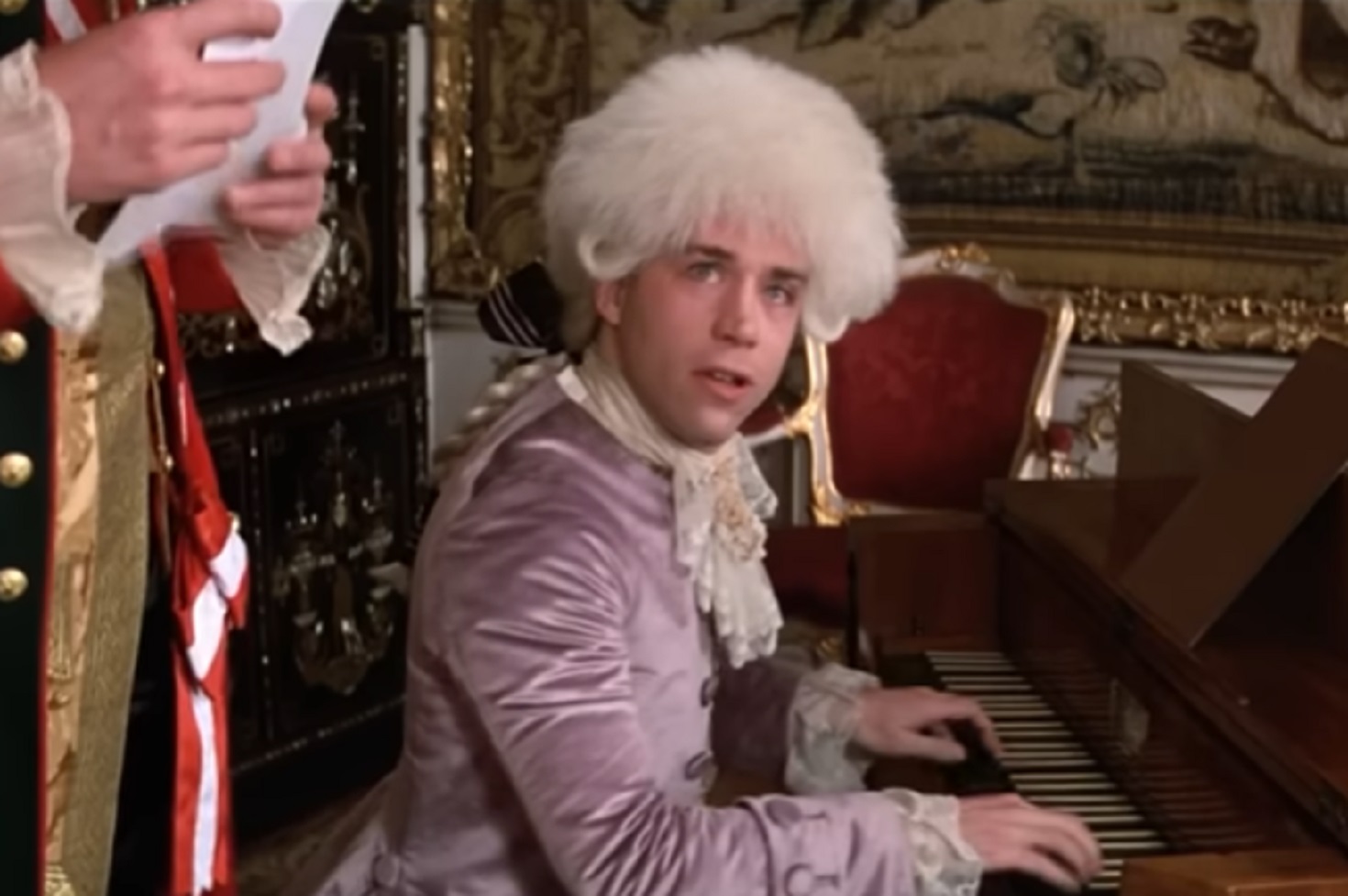 Screenshot: Wolfgang Amadeus Mozart wearing purple jacket is playing on piano - from Amadeus (1984)