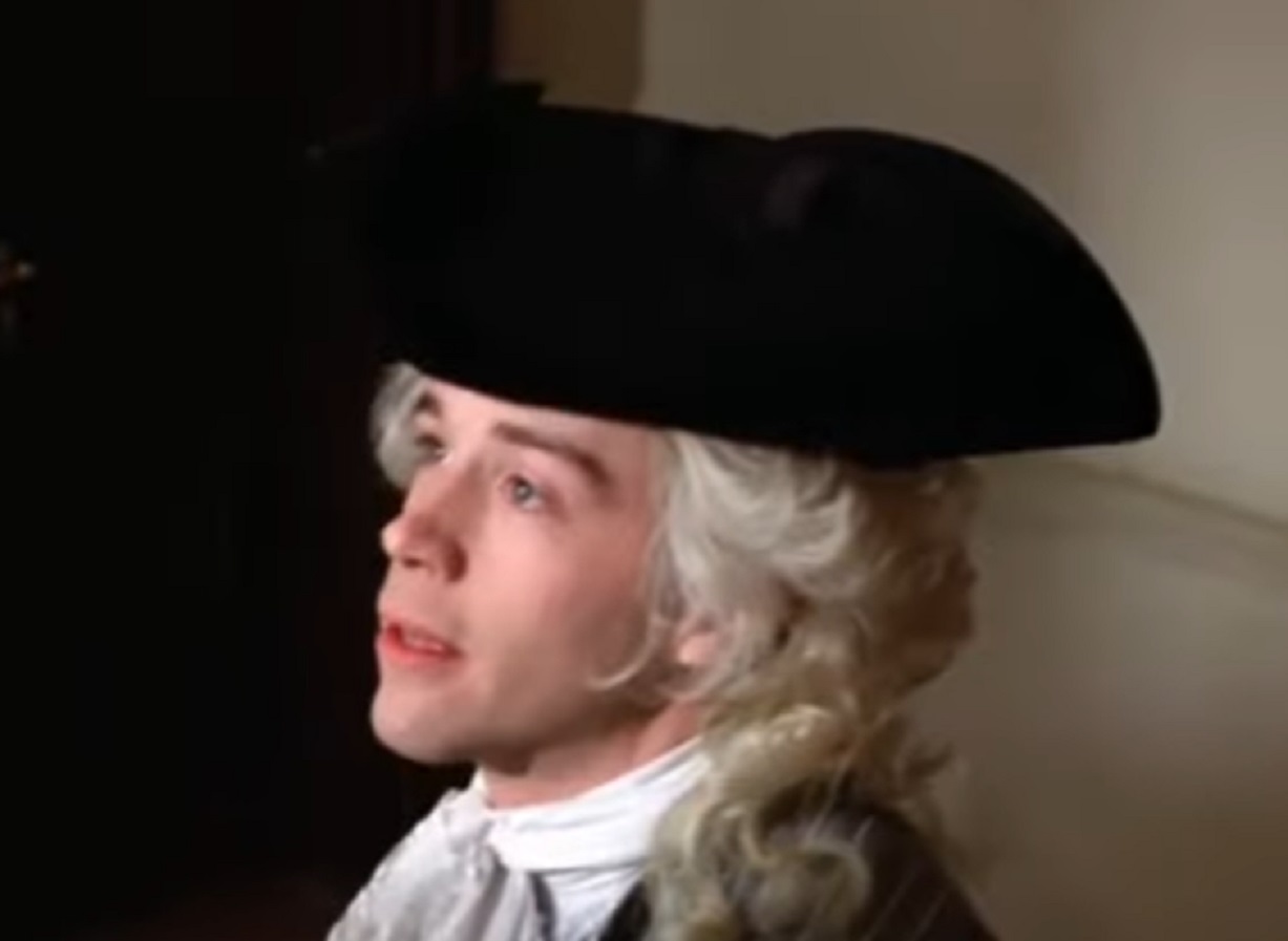Screenshot: Wolfgang Amadeus Mozart with black hat is looking at front - from Amadeus (1984)