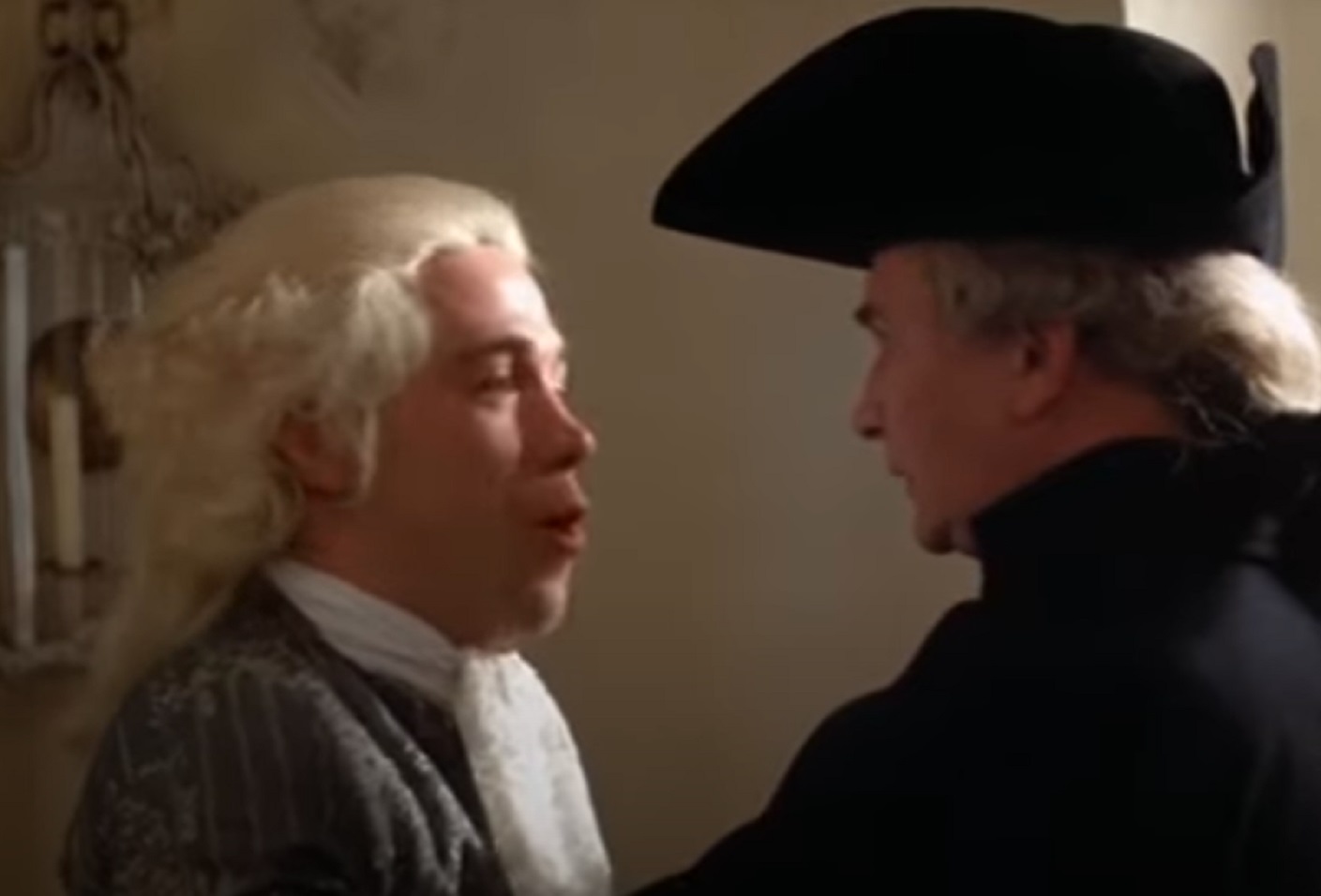 Screenshot: Wolfgang Amadeus Mozart in grey jacket is talking with other male - from Amadeus (1984)