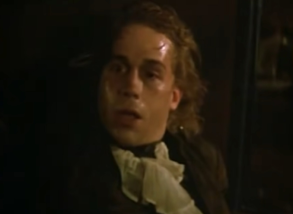 Screenshot: Wolfgang Amadeus Mozart with black jacket is looking at front with sick face - from Amadeus (1984)