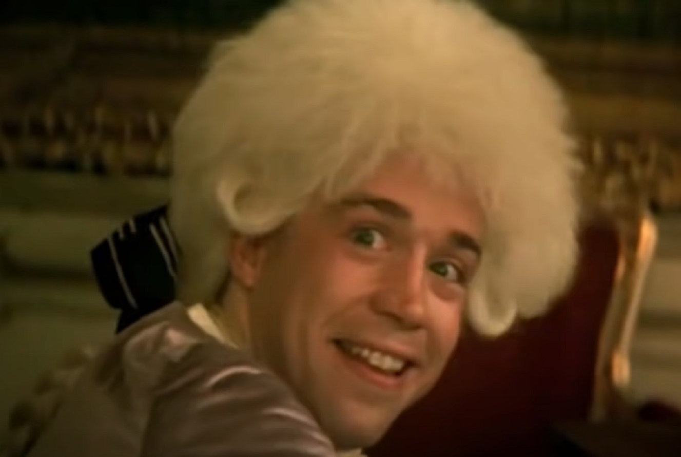 Screenshot: Wolfgang Amadeus Mozart is smiling and looking at back - from Amadeus (1984)