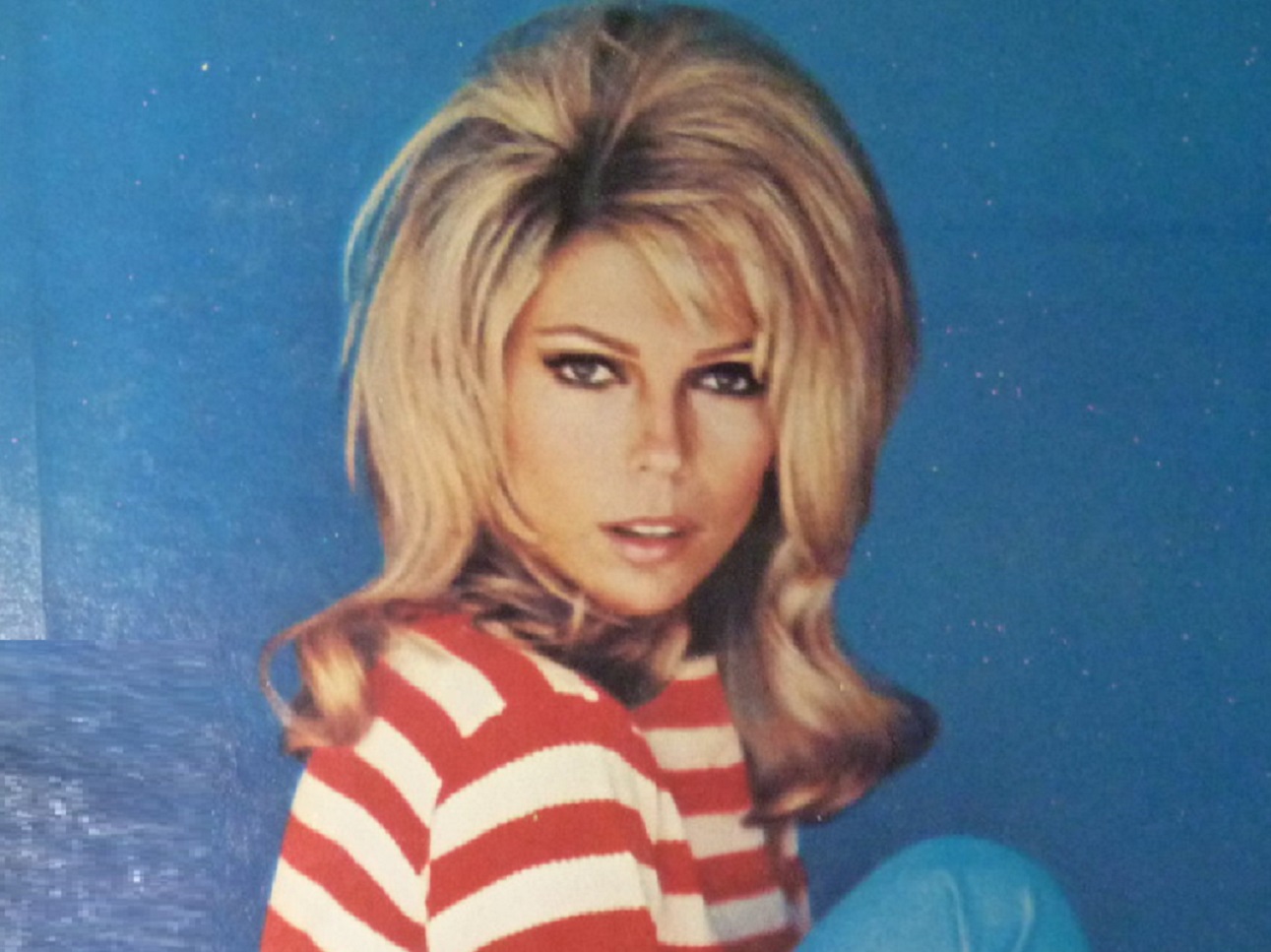 Portrait of Nancy Sinatra looking at camera on blue background.
