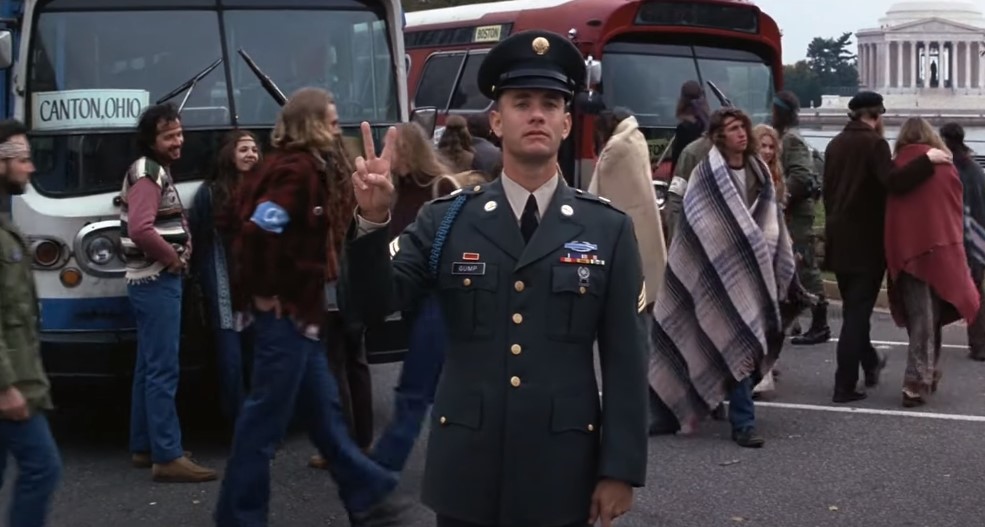 Tom Hanks as Forrest Gump showing peace sing and Hippies walking