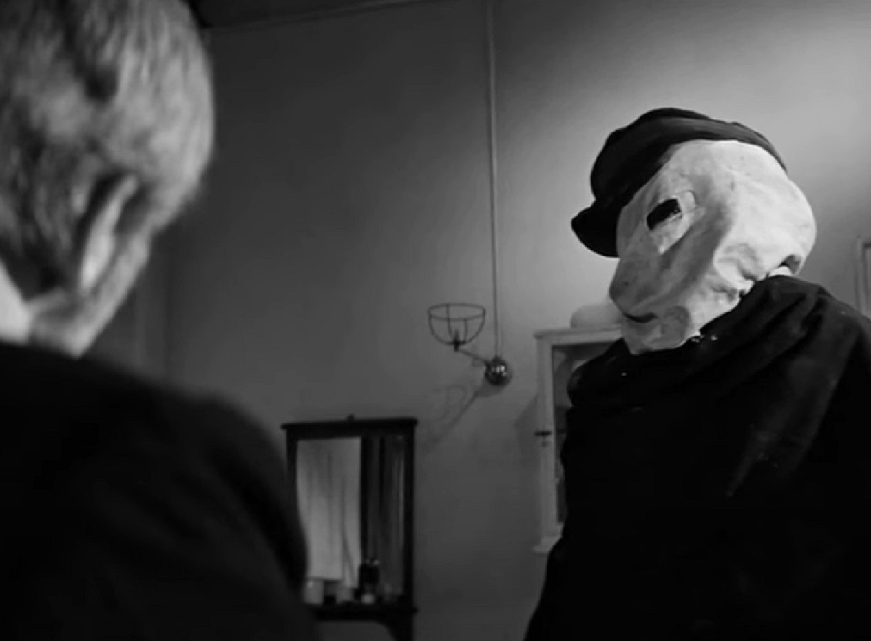 B&W Screenshot of Joseph Merrick (John Hurt) wearing white mask on face and talking - from Elephant Man (1980)