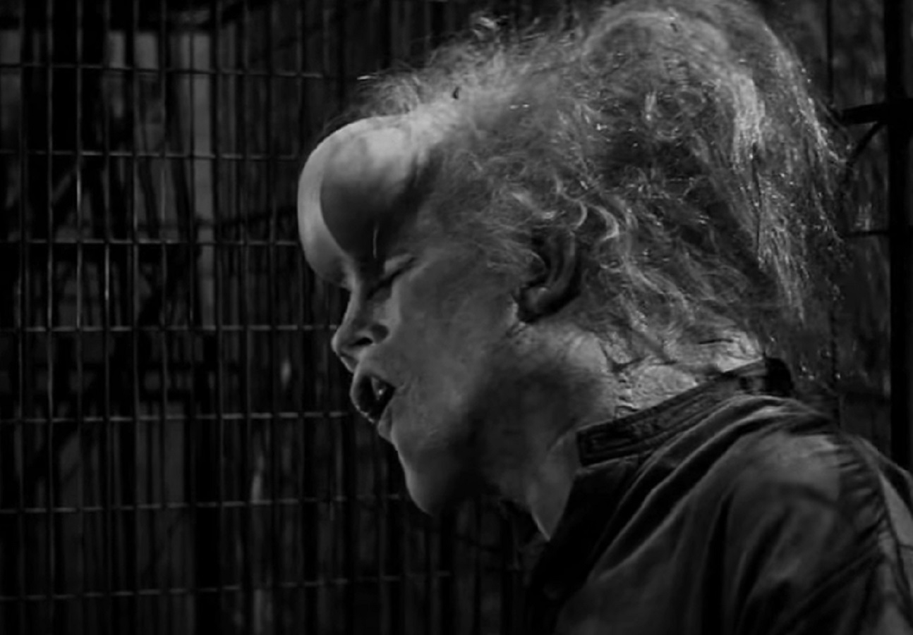 B&W Screenshot of Joseph Merrick (John Hurt) looking at side, seating inside of a cage - from Elephant Man (1980)