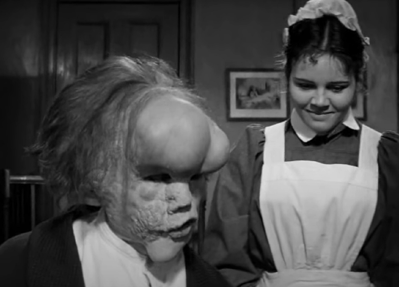 B&W Screenshot of Joseph Merrick (John Hurt) seating next to female servant in room - from Elephant Man (1980)
