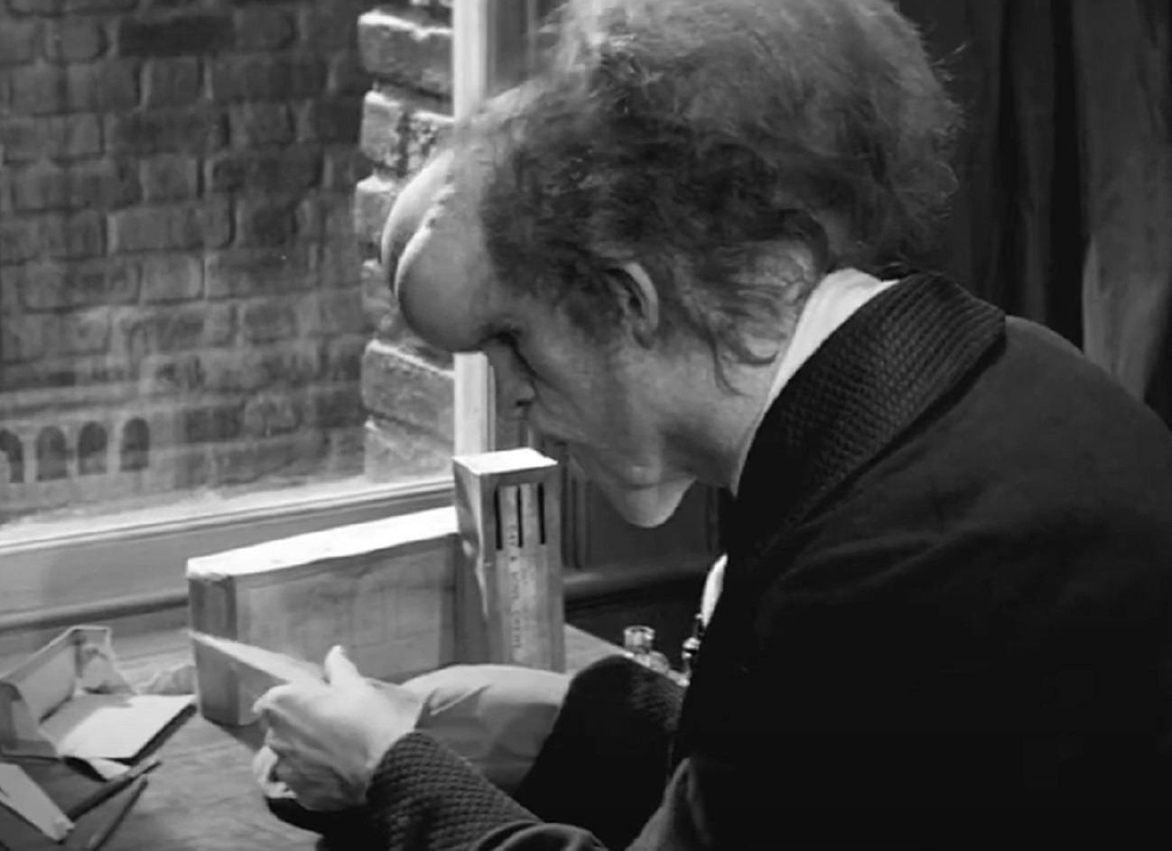 B&W Screenshot of Joseph Merrick (John Hurt) seating on the desk - from Elephant Man (1980)