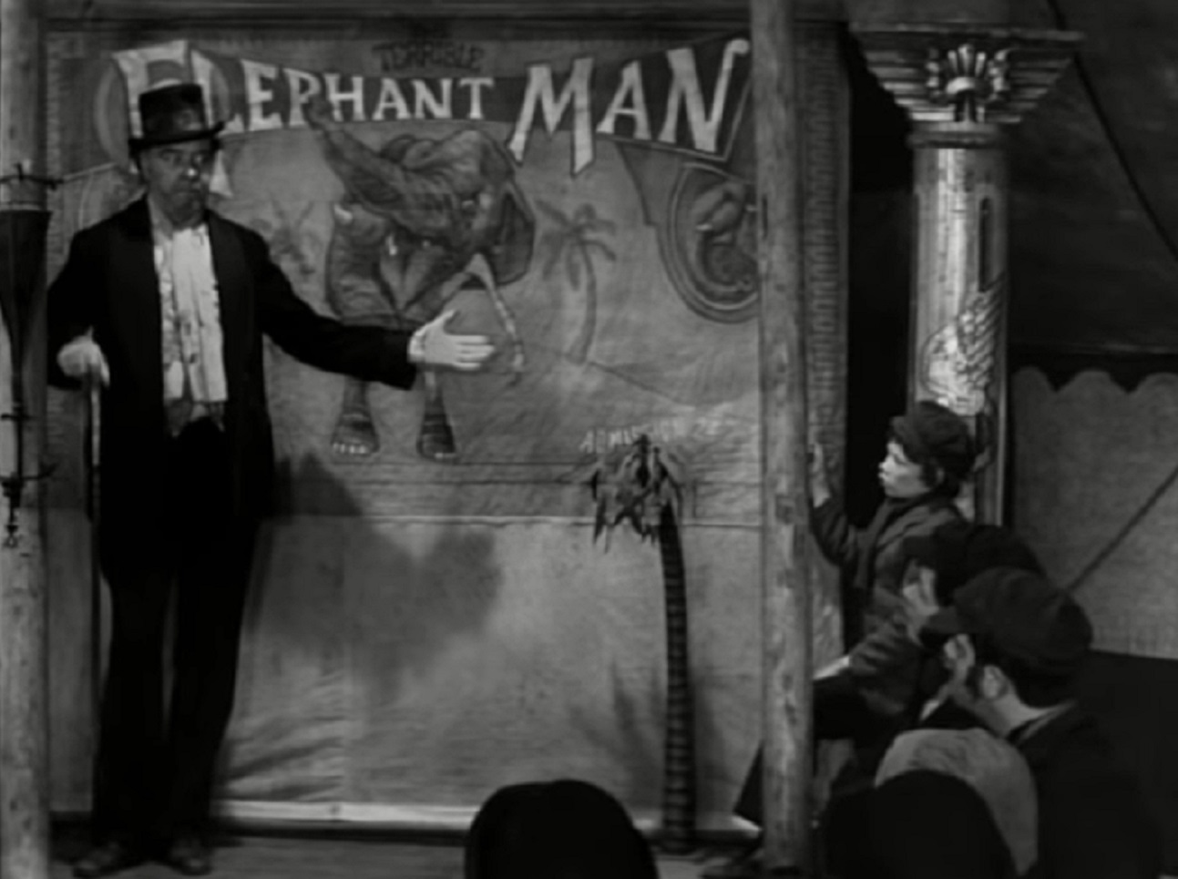 B&W Screenshot of man presenting the Elephant Man on the street - from Elephant Man (1980)