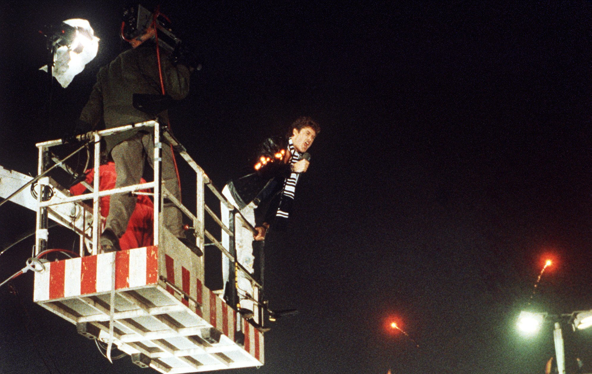 American singer and actor David Hasselhoff hovers in the cage of a hoisting crane above the celebrating people on Berlin Wall and sings 