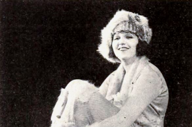 Grayscale Photo of the Actress Bebe Daniels sitting crosslegged on a chair wearing light colored clothes