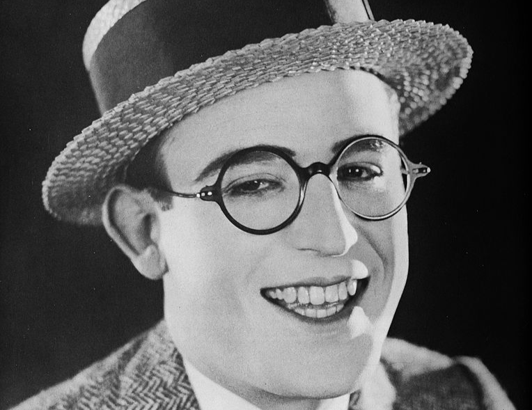 Grayscale Portrait of Harold Lloyd wearing gray suit hat glasses and smiling
