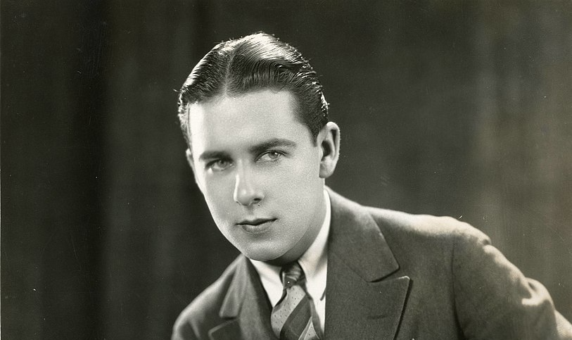 Grayscale Photo of Ben Lyon silent film actor wearing gray suit with a tie