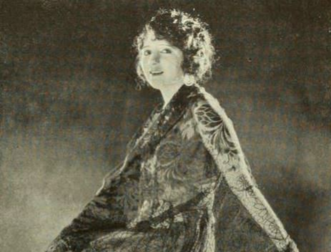 Grayscale Photo of the Actress Bebe Daniels wearing a floral dress sitting on a table