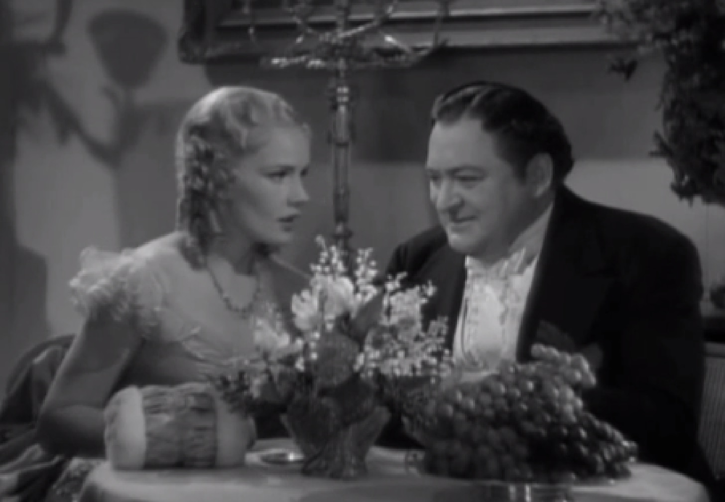 Screenshot of James Fisk (Edward Arnold) and Fleurique (Thelma Leeds) seating on the table - from The Toast of New York (1937)