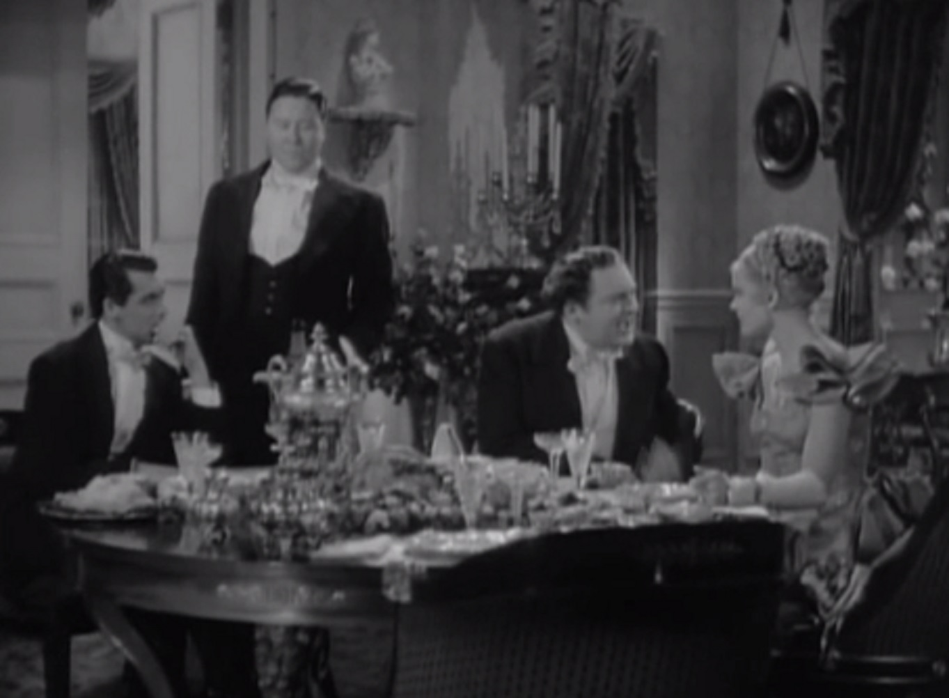 Screenshot of James Fisk (Edward Arnold) and Fleurique (Thelma Leeds) seating on the table and talking - from The Toast of New York (1937)