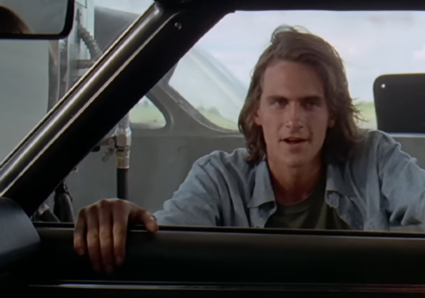 Screenshot of James Taylor outside with long hair in blue shirt - from Two-Lane Blacktop (1971)