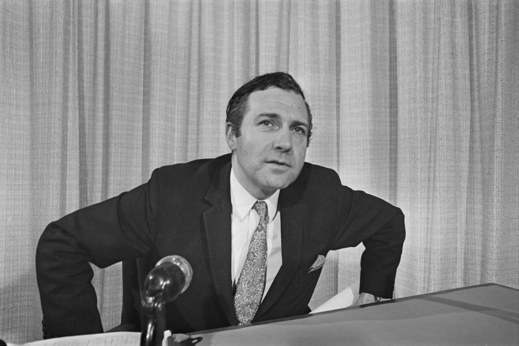 John Stonehouse in suit speaking on a mic