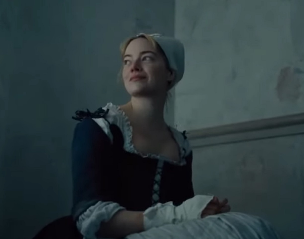 Screenshot: Emma Stone wearing old uniform and hat ,seating on the bed and smiling - from The Favourite (2018)