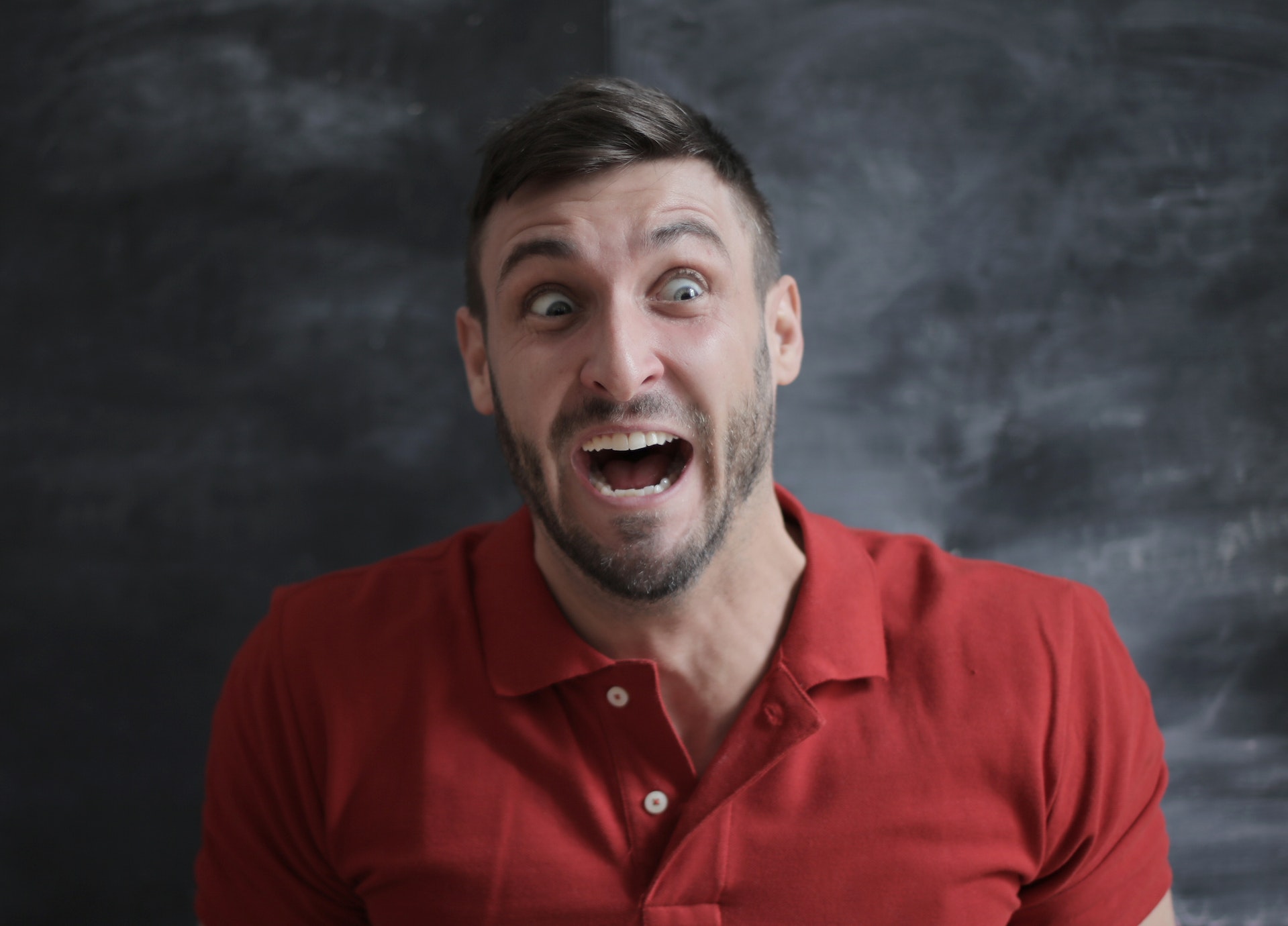 Shocked man in red polo shirt standing in front of a gray background