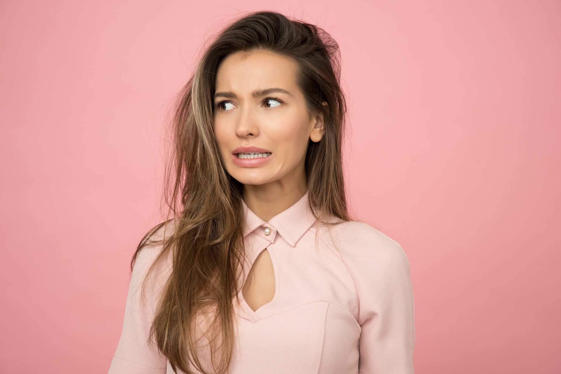 Scared woman in pink top standing in front of pink background