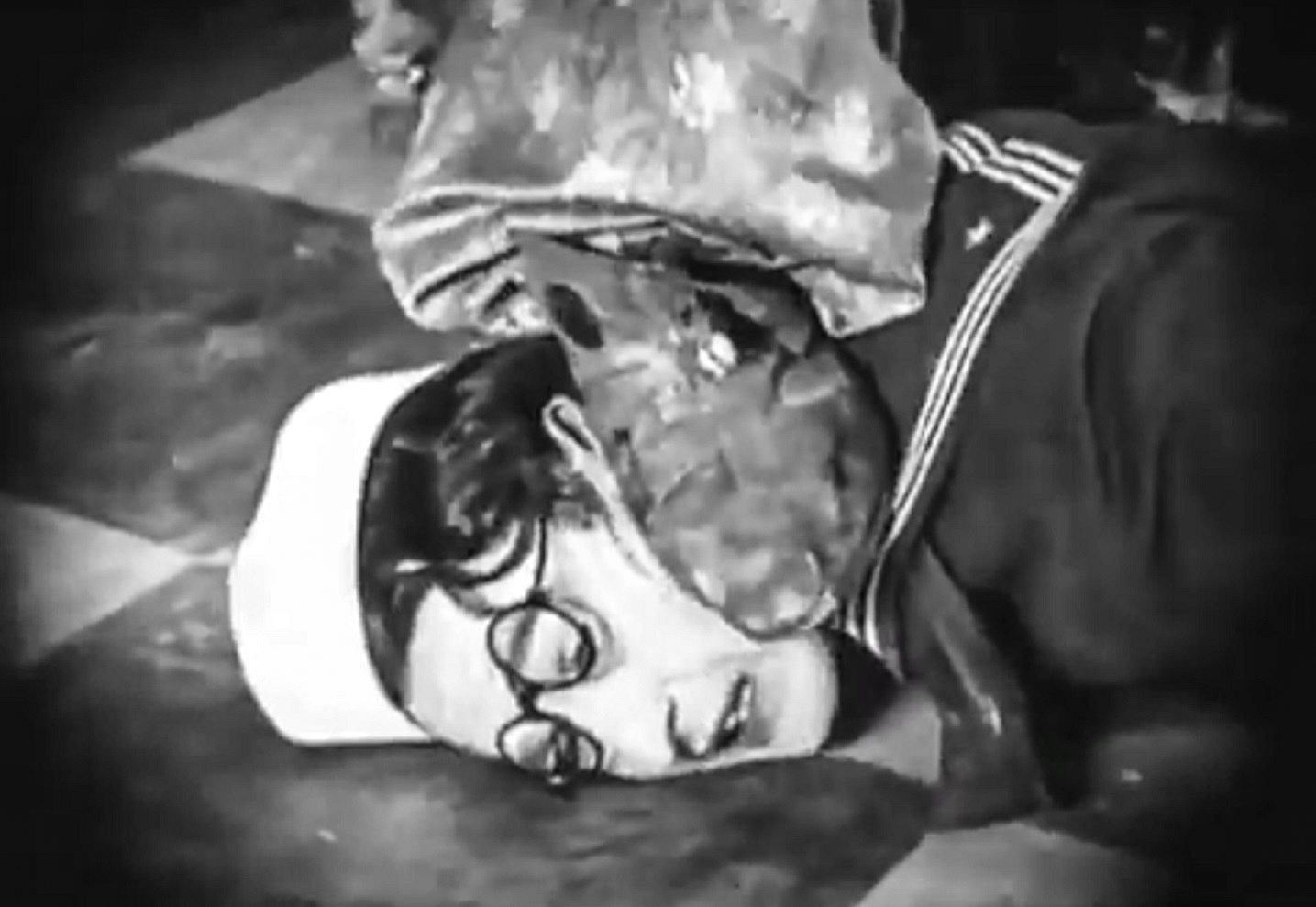 Screenshot B&W - Harold Lloyd wearing navy suit laying on the floor with someone's foot on his head  - from A Sailor-Made Man (1921)